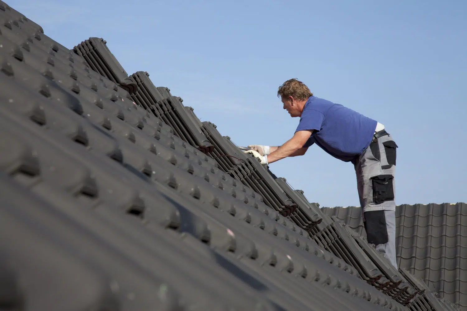 A roofer installing dark gray roof tiles on a steep roof pitch. Hendersonville TN Roofing Installation by Burish Builder TN.