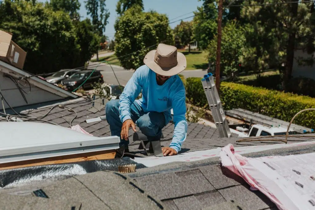 A professional roofer wearing a wide-brimmed hat working on installing or repairing a residential roof with shingles and exposed underlayment, illustrating expert Nashville TN Residential Roofing Services by Burish Builder TN.