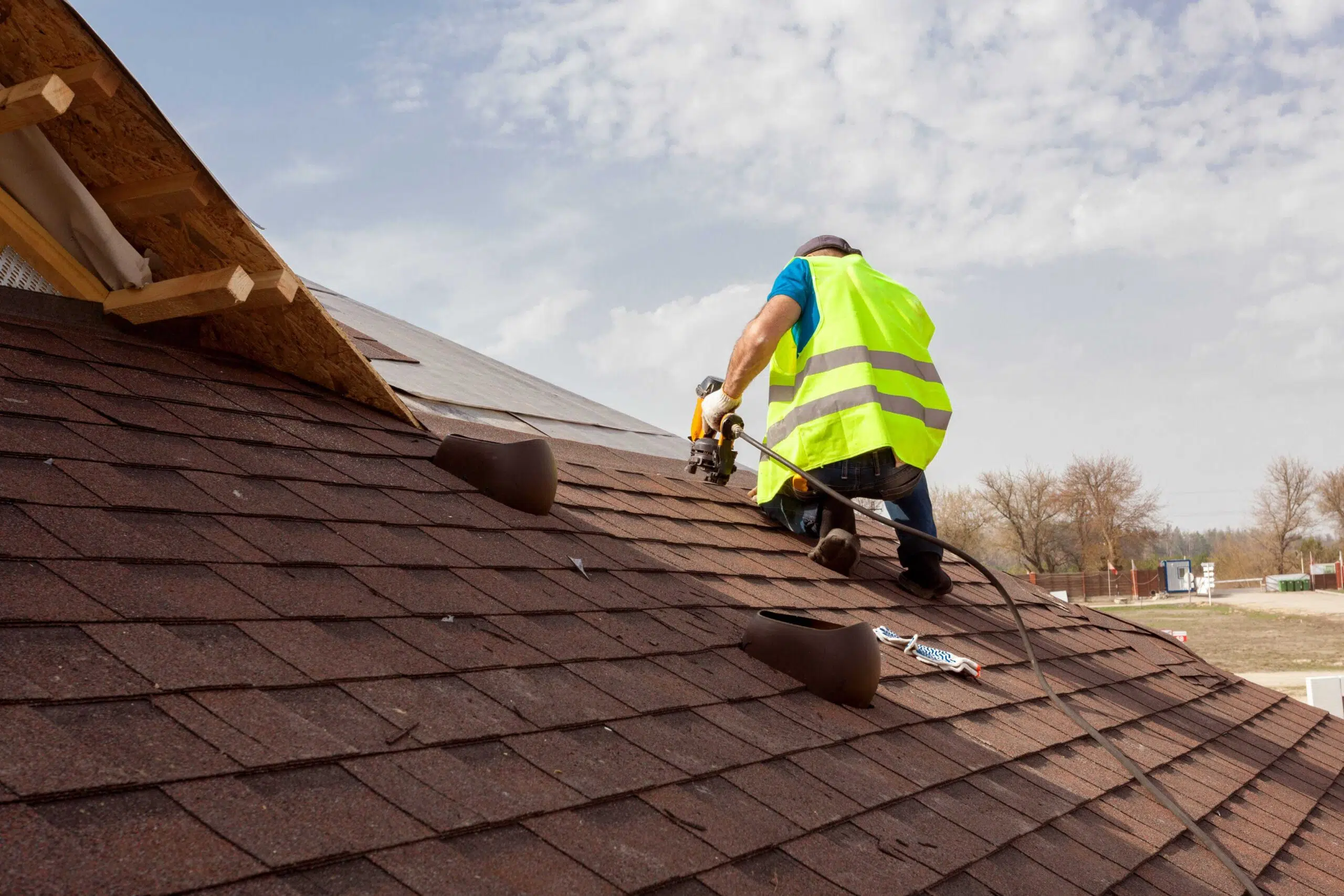 Roofing Installation Brentwood TN by Burish Builders TN. Roofer in a safety vest nailing brown asphalt shingles on a sunny day.