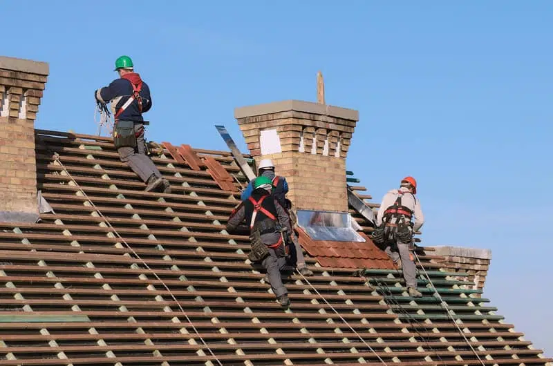 Roofers with safety harnesses working on a steep, multi-level roof for a Roofing Replacement Brentwood TN project by Burish Builders TN.